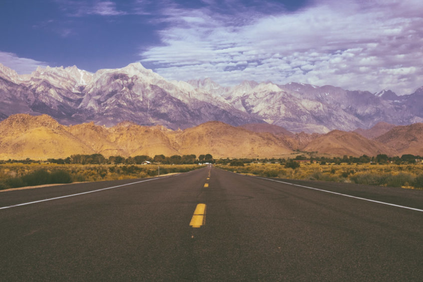 endless road with yellow cliffs green grass and huge white mountains covered with snow