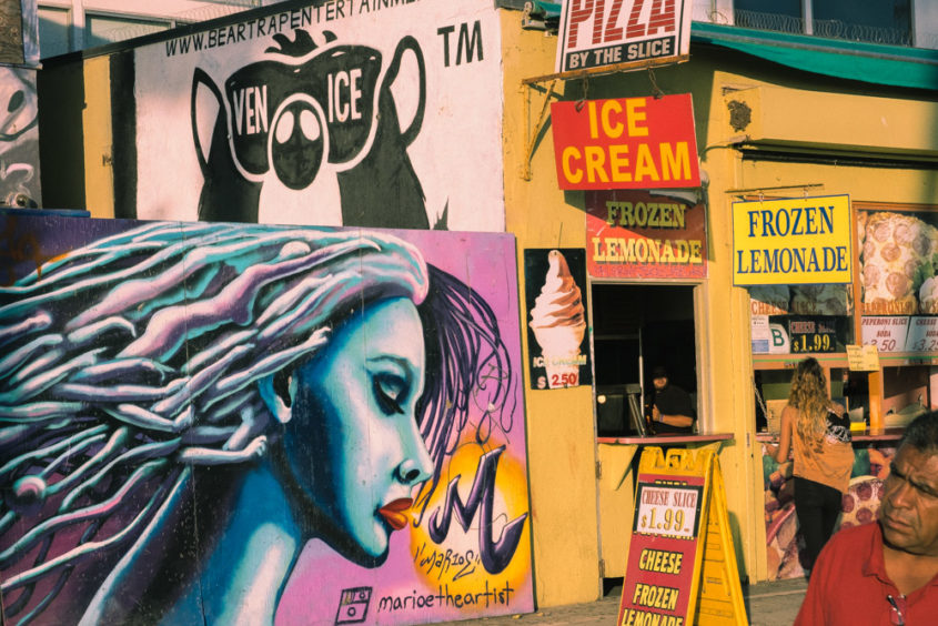 girl painting on the wall and yellow building with food and restaurant signs and a man walking in the corner