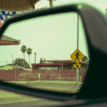 View from car mirror with palm trees and street sign