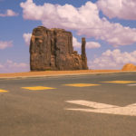 One of the three sisters of monument valley with a street view, crossing sign and arrow