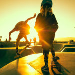 Young skater girl watching skater jump with the sunset view at the skate park