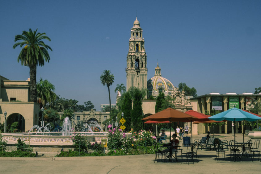 balboa park view with palm trees red umbrellas and people in front of a fountain
