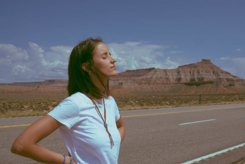 girl with eyes closed on empty american road with mountains