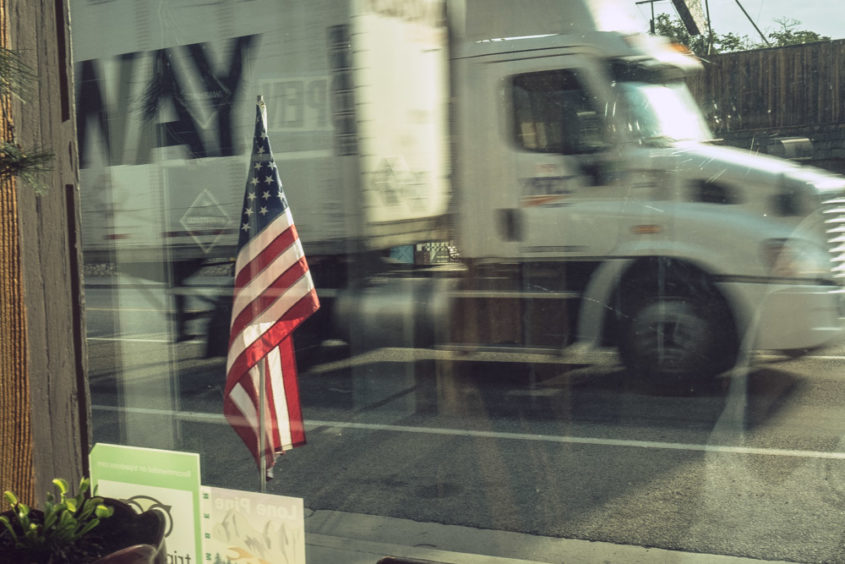 view from shop window of american flag and moving white truck