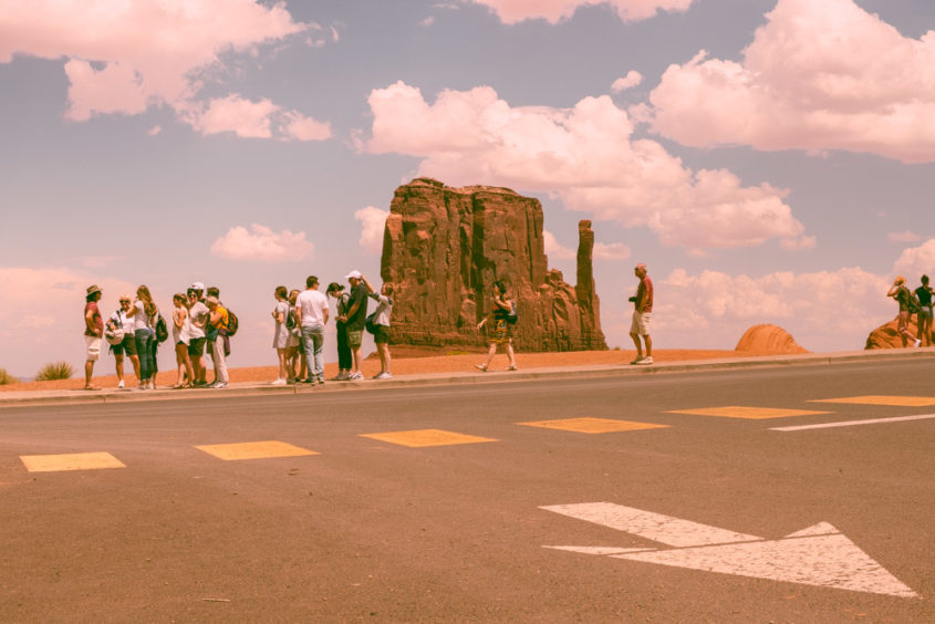 street with white arrow painted and yellow squares and tourists walking down red cliff