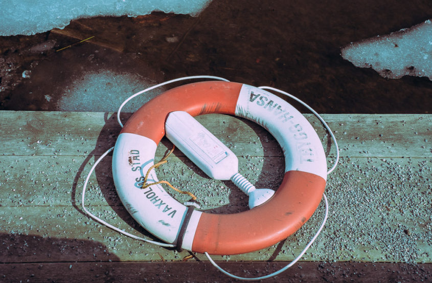 red and white life buoy on wooden deck with dark water and ice 