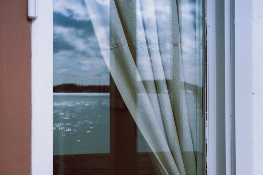 window reflection with white curtain and water and island in the back